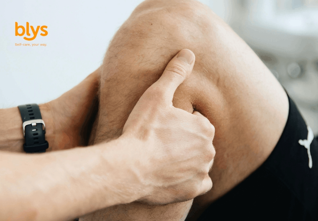A sports massage therapist gently holds a runner's bent knee, with a black smartwatch on their wrist; the close-up conveys attentive self-care, alongside the orange “Blys” logo.