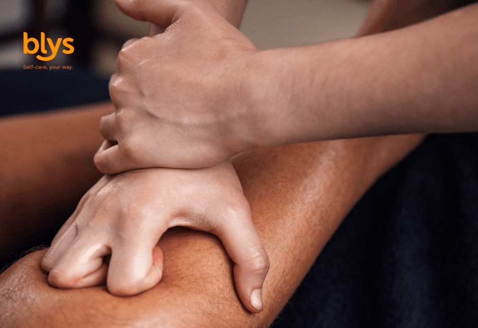 Close-up of hands applying firm massage pressure to a person, conveying relaxation, wellness, and therapeutic self-care; Blys logo visible.