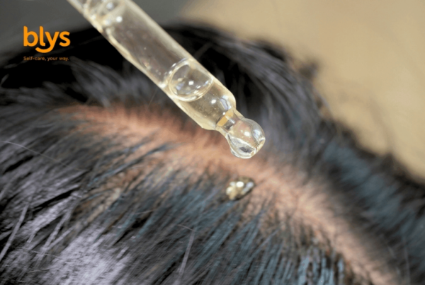 Close-up of a dropper releasing clear serum onto an exposed scalp between dark hair strands, suggesting a focused, soothing scalp treatment.