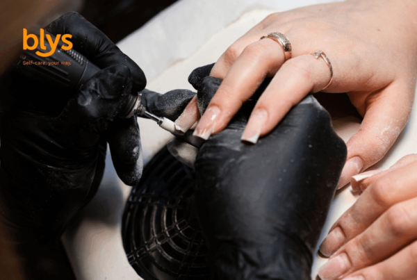 Close-up of a nail technician in black gloves performing Russian manicure with an electric file on a client’s long manicured nails, conveying precision and care.