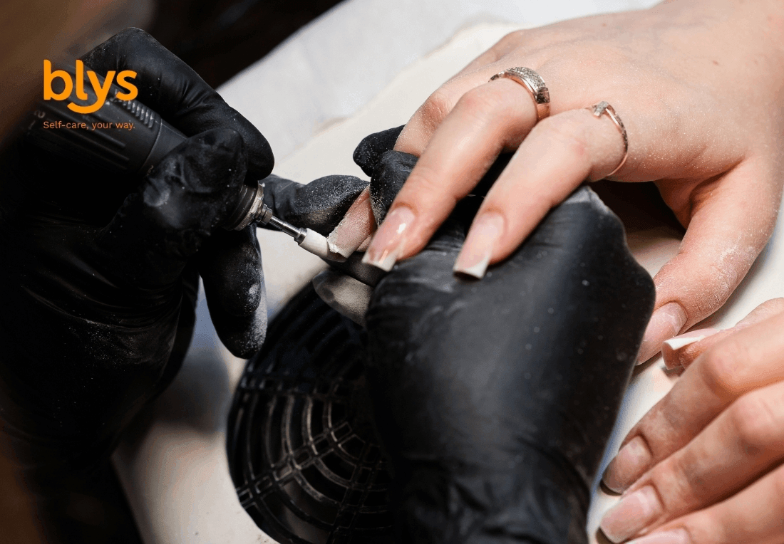 Close-up of a nail technician in black gloves performing Russian manicure with an electric file on a client’s long manicured nails, conveying precision and care.