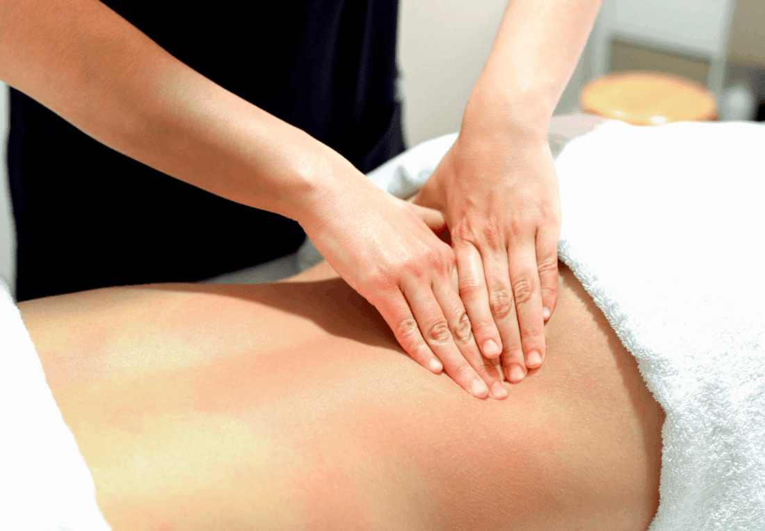 A massage therapist gently presses both hands into a client’s bare lower back for ql pain on a treatment table, conveying calm, soothing relaxation in a room setting.