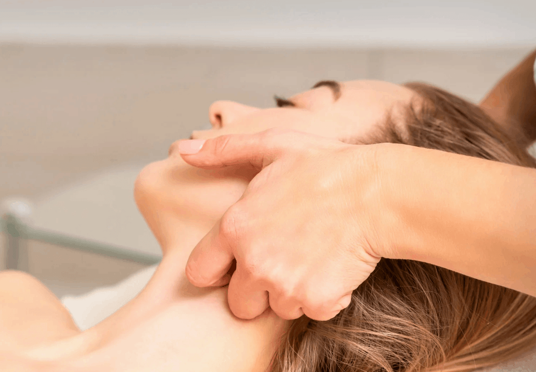 A massage therapist gently massages a woman’s face and jaw as she reclines with eyes closed, creating a calm, soothing TMJ treatment scene.